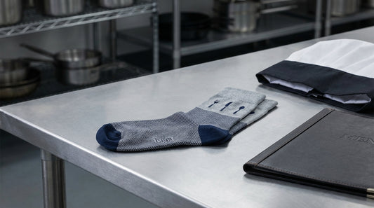 Custom restaurant-branded socks arranged next to a chef hat and menu on stainless steel