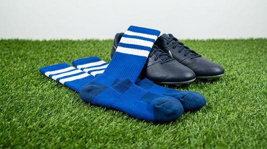 Custom football socks in team colors laid out on turf with cleats, showing over-the-calf length and reinforced heel construction