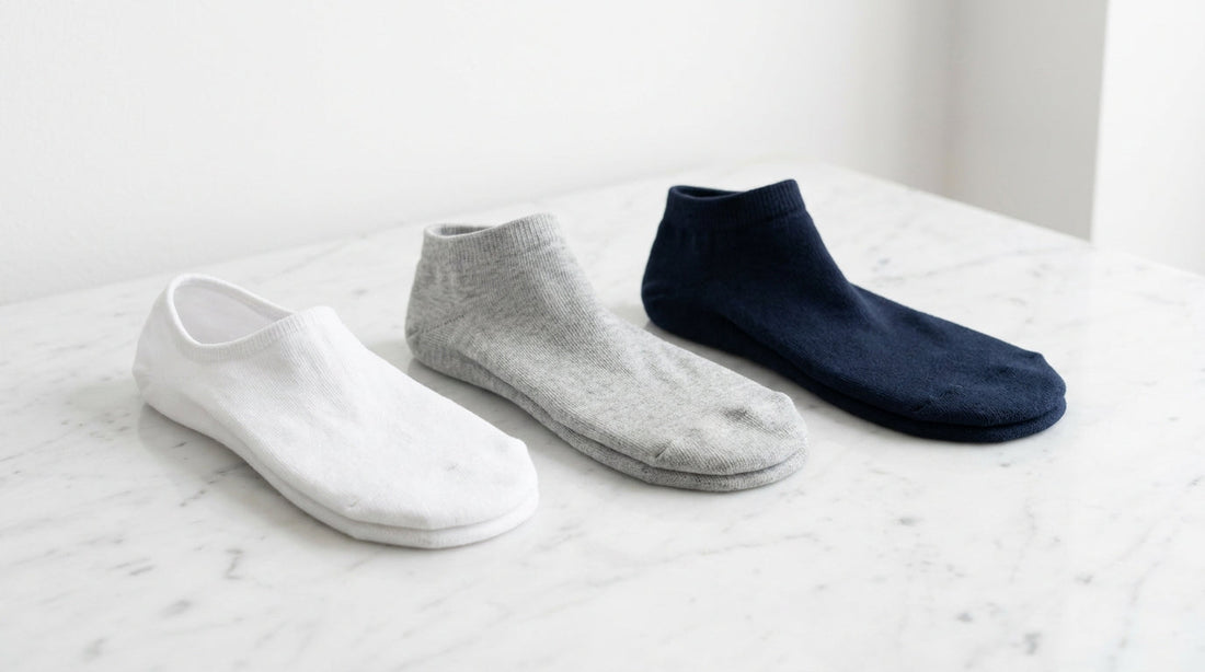 A row of three low-cut sock styles in white grey and navy on a clean marble surface showing different cuff heights
