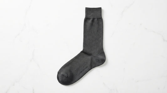 Premium dress sock laid flat showing six quality details: fine-gauge knit texture, reinforced heel, seamless toe, ribbed cuff, fabric sheen, and branded sole