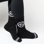 Woman wearing black crew socks with SIP circled on the leg kneeling to tie shoe