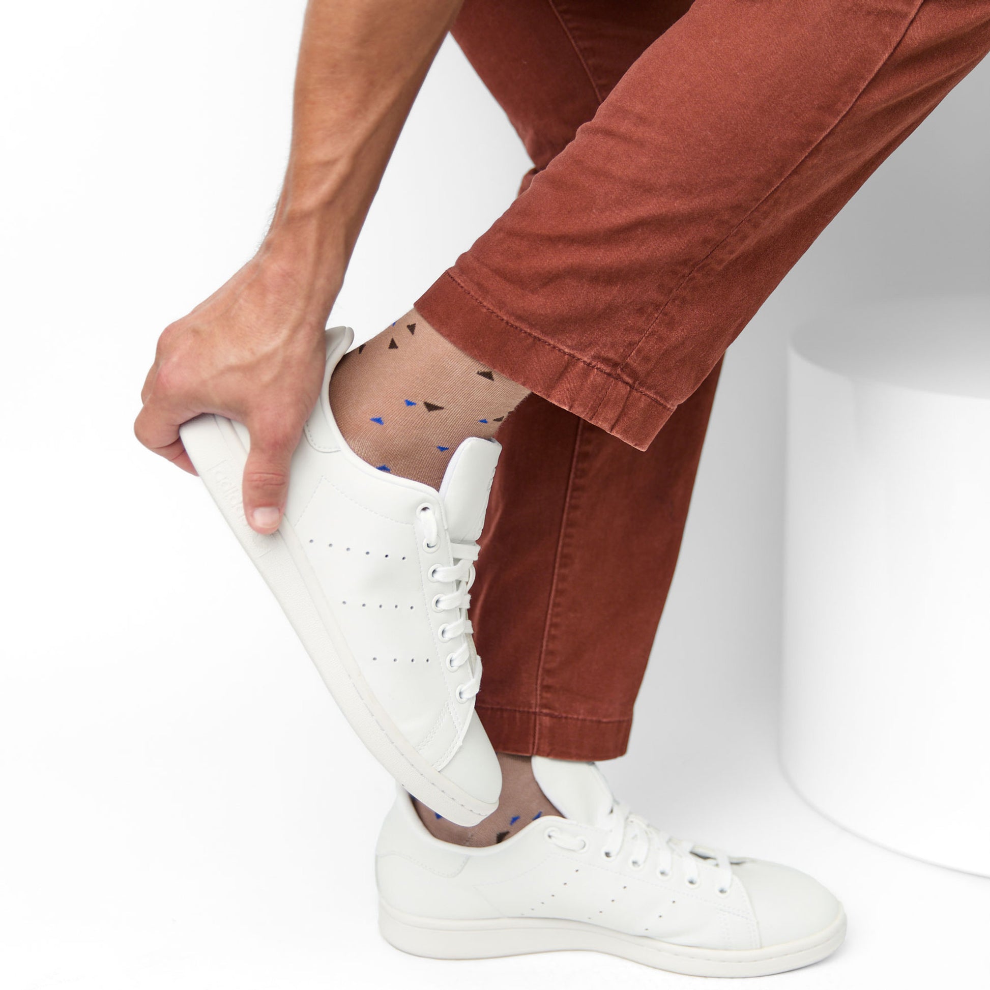 Light brown dress sock with small chicklet triangle designs in navy blue and dark brown worn with red pants and white shoes.