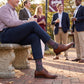 MSU Gray Cowbell Dress socks worn seated, showing scattered maroon cowbells and the interlocking MSU logo on charcoal