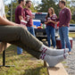 Gray M-State Logo Casual socks worn seated on campus, third angle, showing the maroon M-STATE banner logo on a heather-gray crew