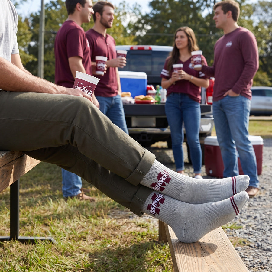 Gray M-State Logo Casual socks worn seated on campus, third angle, showing the maroon M-STATE banner logo on a heather-gray crew