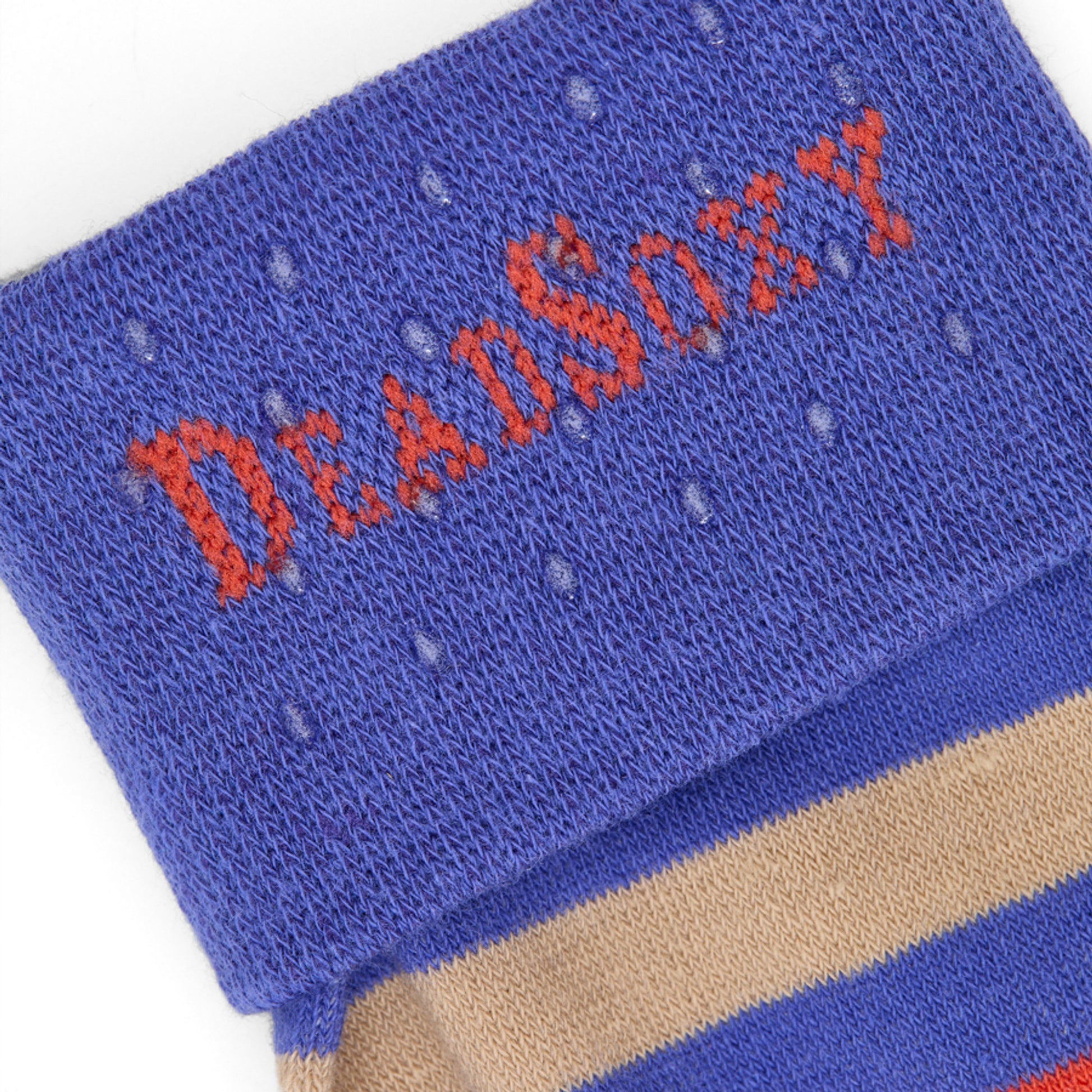 Close-up of DeadSoxy logo on royal-blue TrueStay‚Ñ¢ cuff with silicone grip dots on Jones bold striped sock.