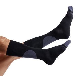 1 black dress sock with a large circle on the back of the leg and 2 charcoal accent stripes around the toe shown on legs coming into the image from the left