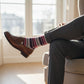 Leon dress socks worn with crossed legs, showing maroon and navy stripes in a lifestyle setting.