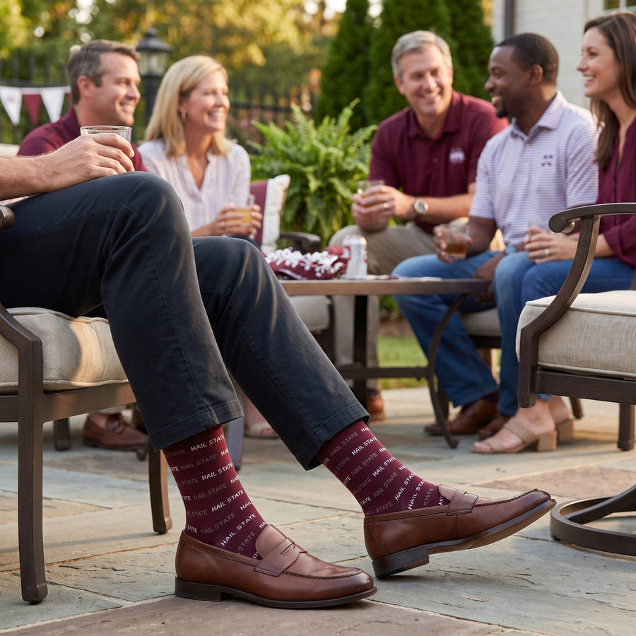 MSU Hail State Dress socks worn seated, showing repeating HAIL STATE text in white and gray on maroon