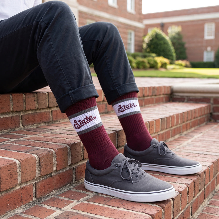 MSU Retro Script Casual socks worn seated on campus, showing the State script on a white band across a maroon crew