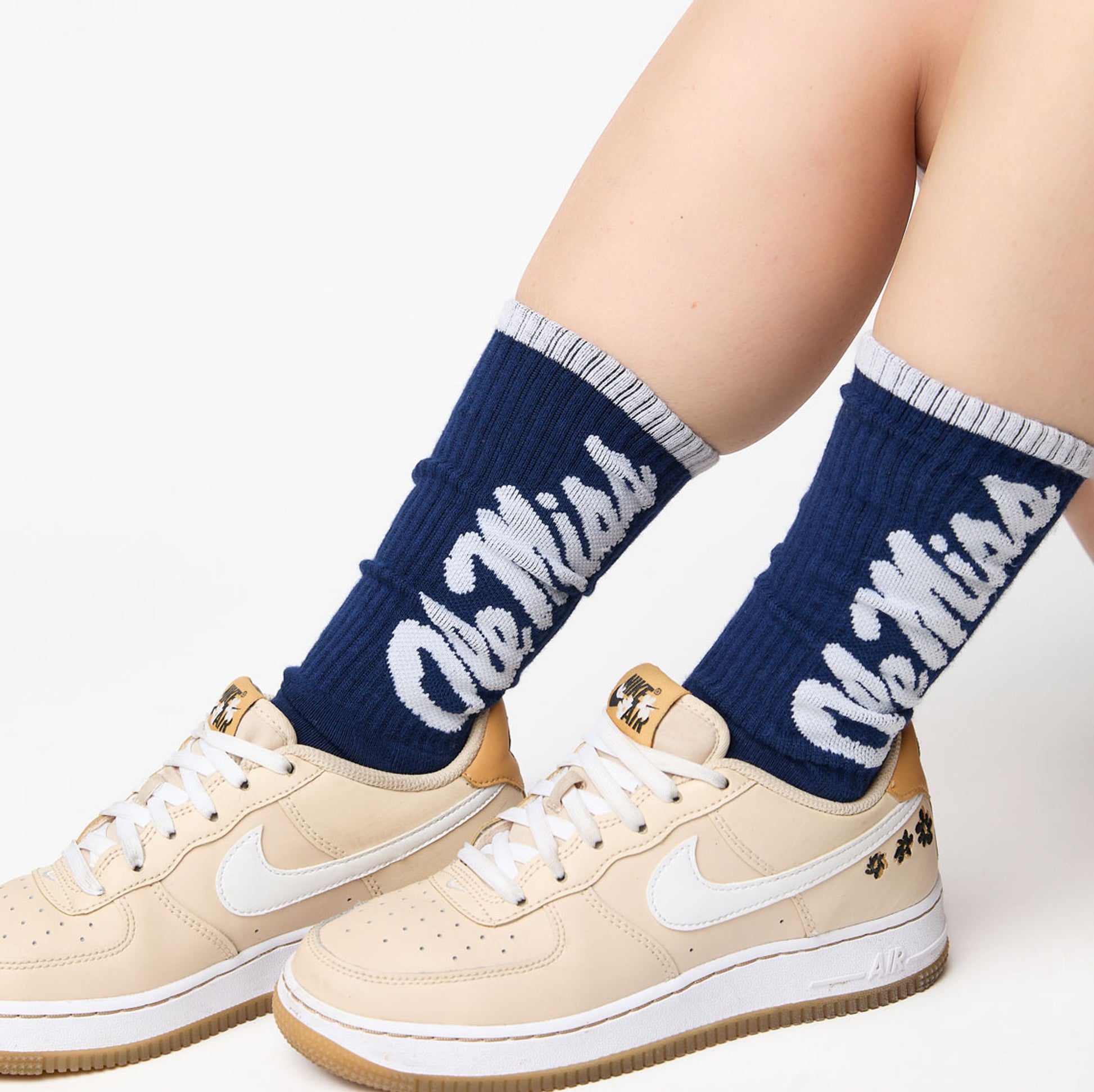Navy casual crew socks with Ole Miss going up the leg in white worn with cream sneakers by a women.