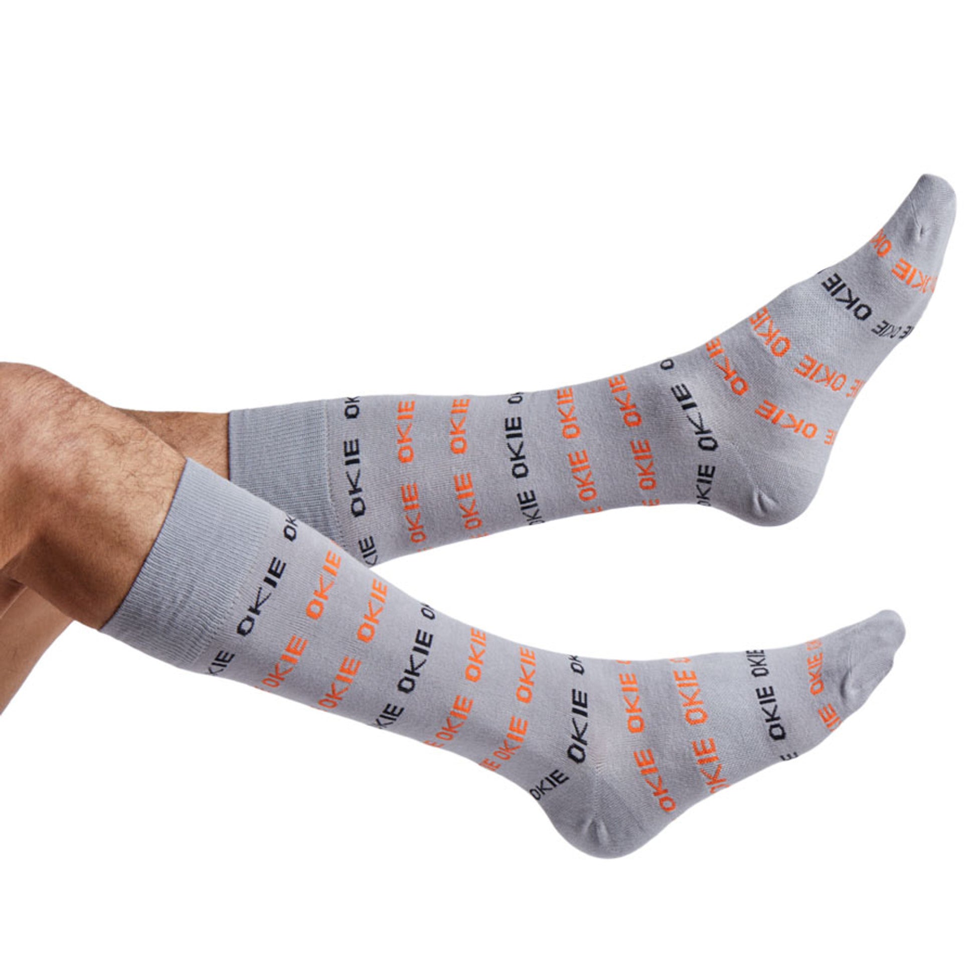 Grey dress sock with OKIE in orange and black shown feet coming into the left side of the image.