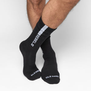 Black casual crew socks with ‚ÄúREBELS‚Äù written in white down of the leg on male model with legs crossed