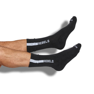 Black casual crew socks with ‚ÄúREBELS‚Äù written in white down of the leg on male model with legs straight