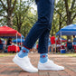Person wearing blue socks with a logo, standing on a brick path with trees and people in the background.