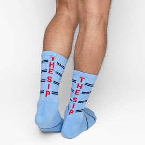 Powder blue athletic casual crew socks with double navy blue stripes and "THE SIP" written up the back of the leg shown on male model.