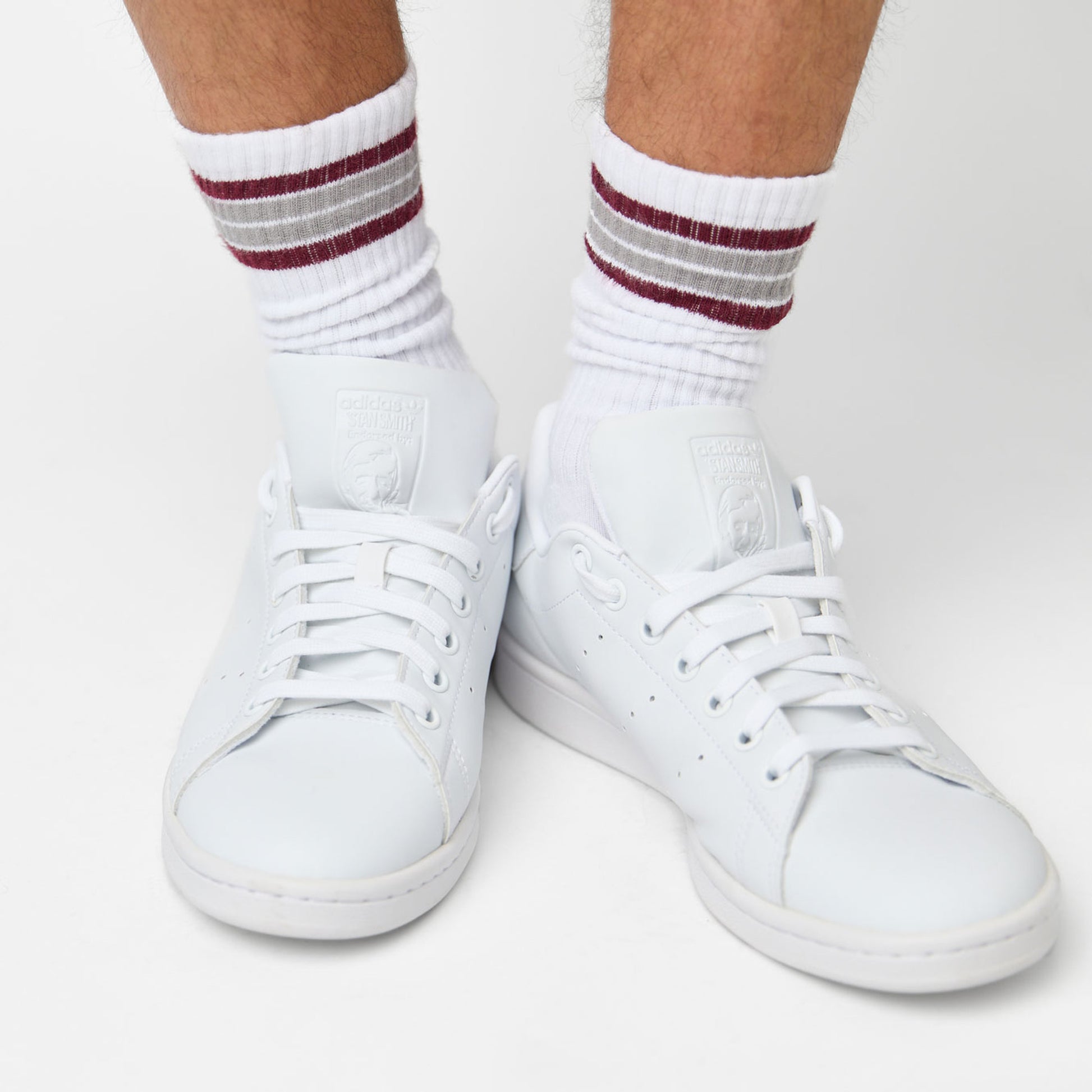 White casual crew socks with 4 thin stripes on the top in maroon and grey shown on a female model from  a distance