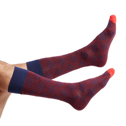 1 red dress sock with navy blue bigger diamonds made of smaller diamond dots shown on legs coming into the image from the left