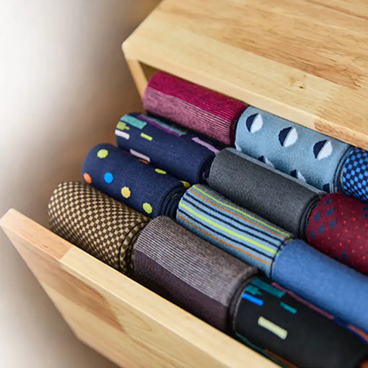 A collection of neatly rolled men’s dress socks in various patterns and colors, including solid hues like navy blue and gray, as well as vibrant designs with polka dots, stripes, and geometric shapes.