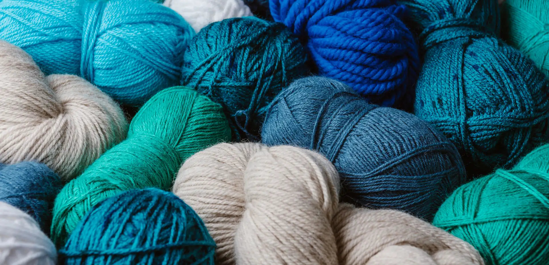 A collection of skeins in various shades of blue, teal, and cream-colored yarn.
