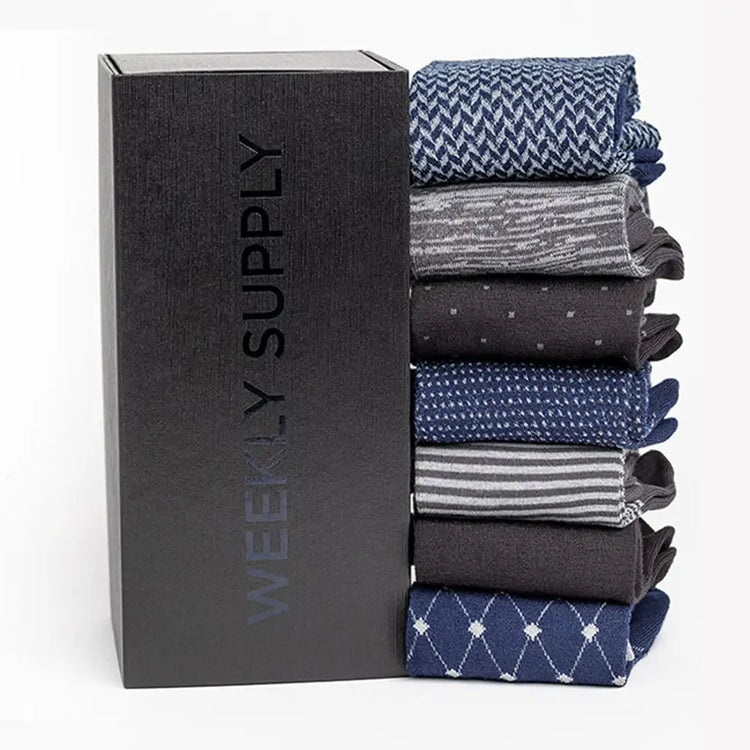A neatly stacked set of six men’s dress socks in various patterns and shades, including navy blue with white herringbone, gray heathered stripes, dark charcoal with small dots, solid black, light blue with fine polka dots, and another