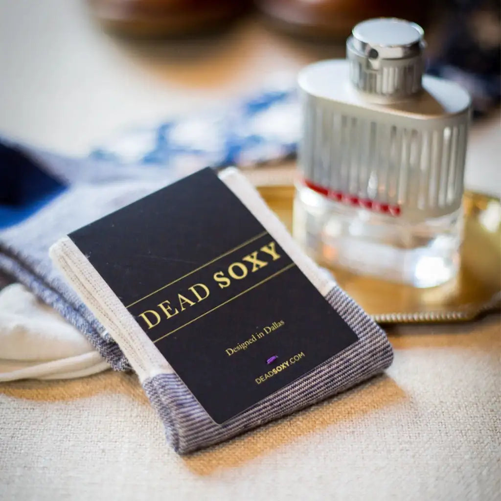 A pair of gray and white striped socks with a black label that reads ’dead soxy’ in gold lettering.