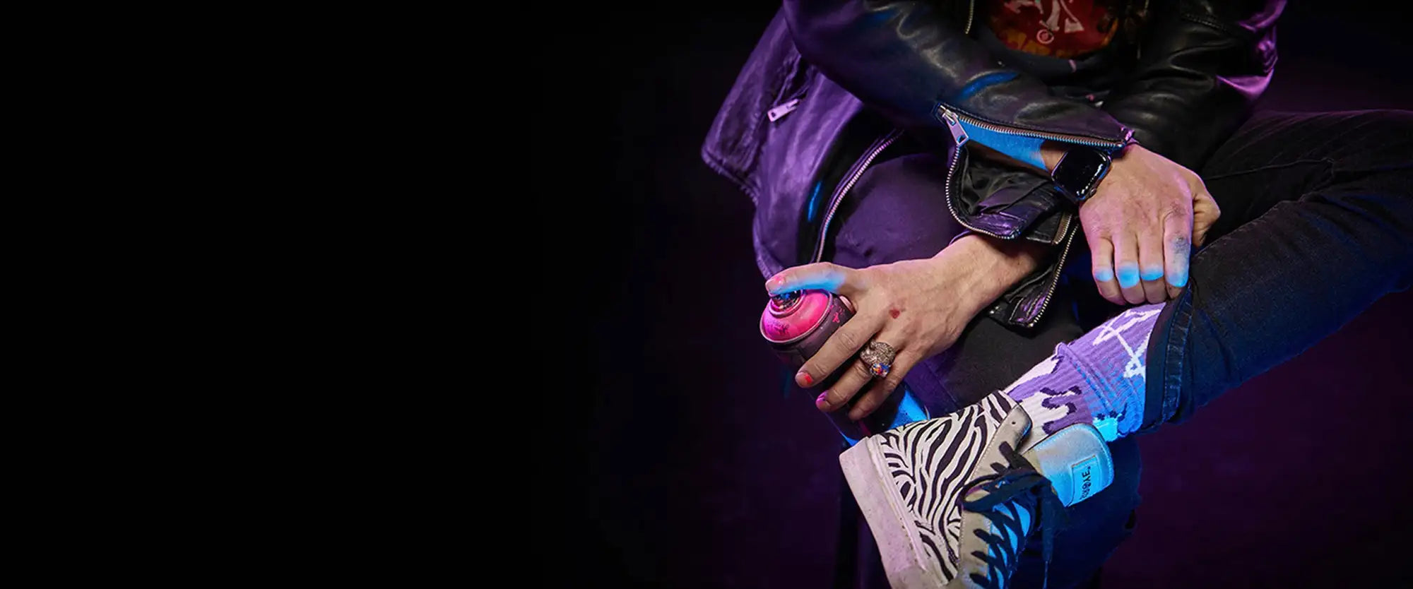 Pink spray paint can with a blue nozzle and silver cap, held in hand against dark background
