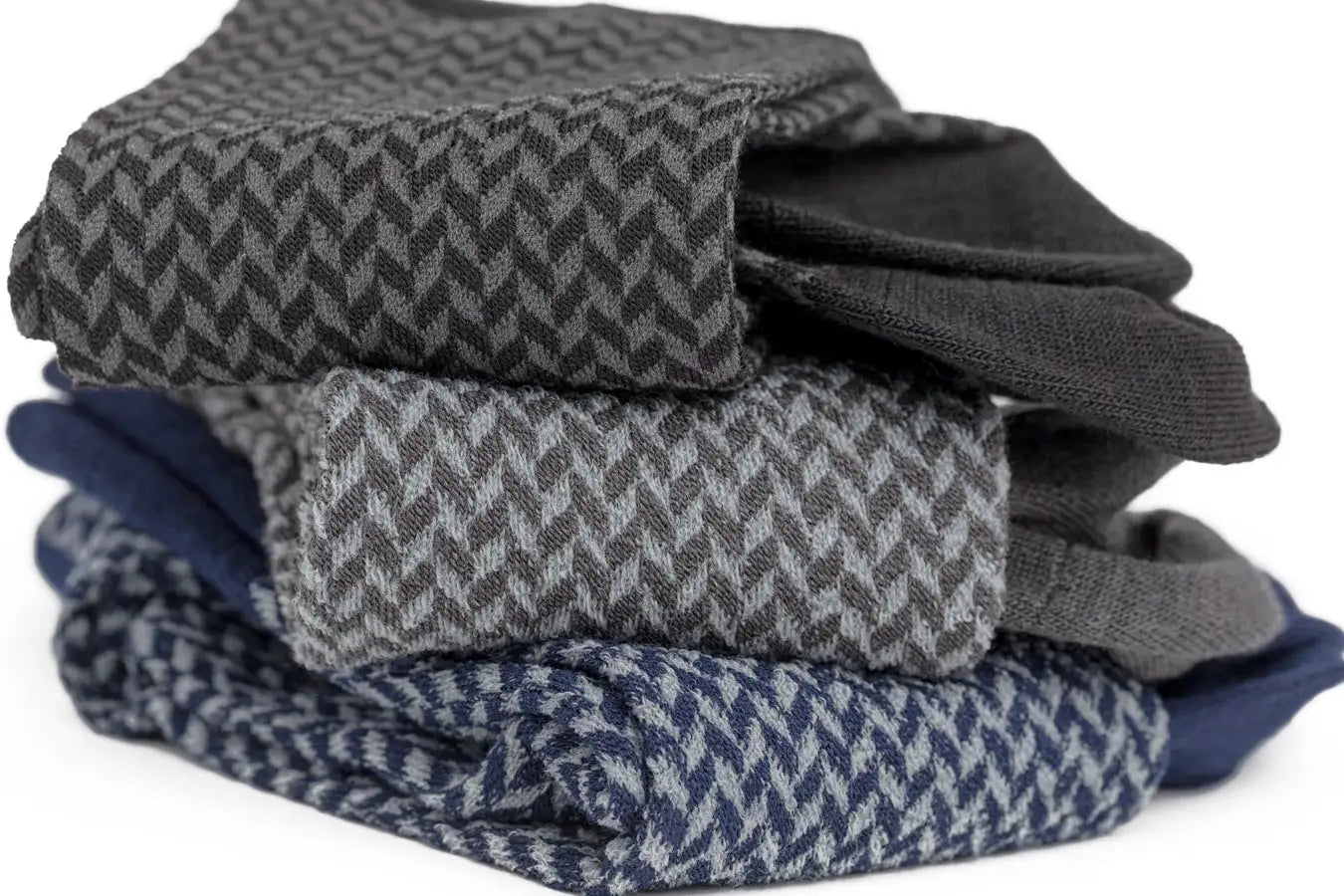 Stack of folded men’s herringbone socks in gray, navy blue, and charcoal tones.