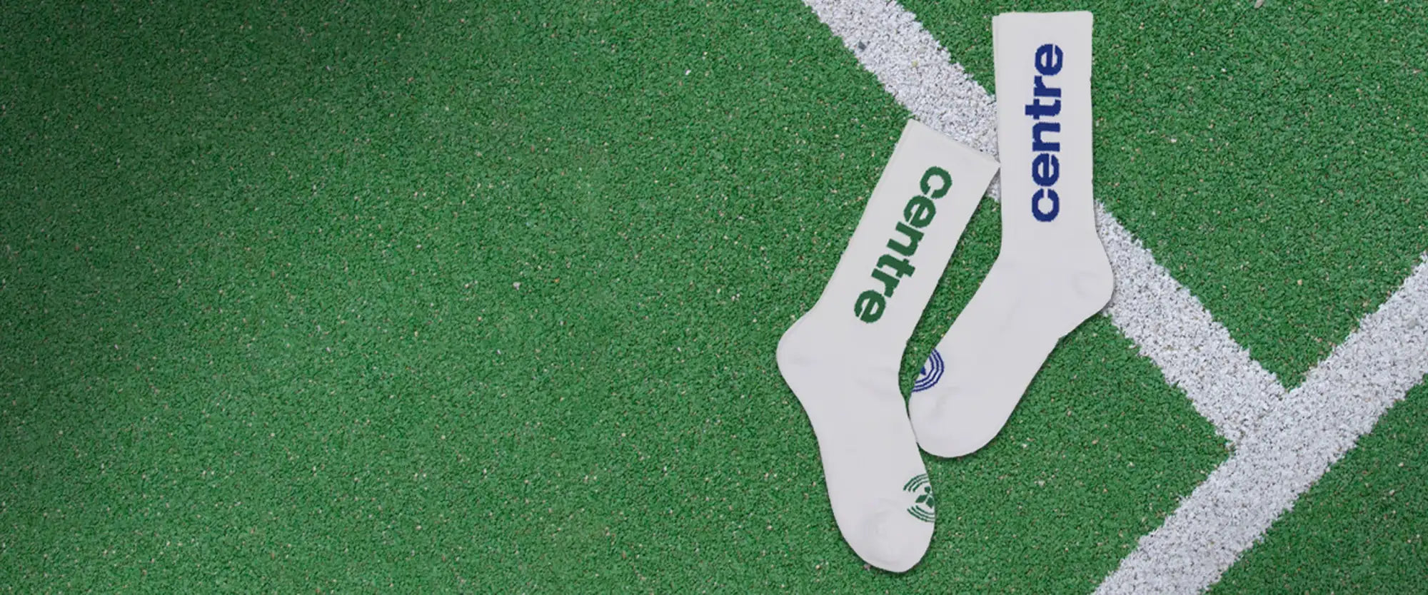 White athletic socks with ’centre’ printed in green and blue lettering, featuring a small circular logo near the toe.