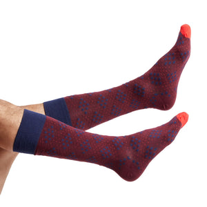 1 red dress sock with navy blue bigger diamonds made of smaller diamond dots shown on legs coming into the image from the left